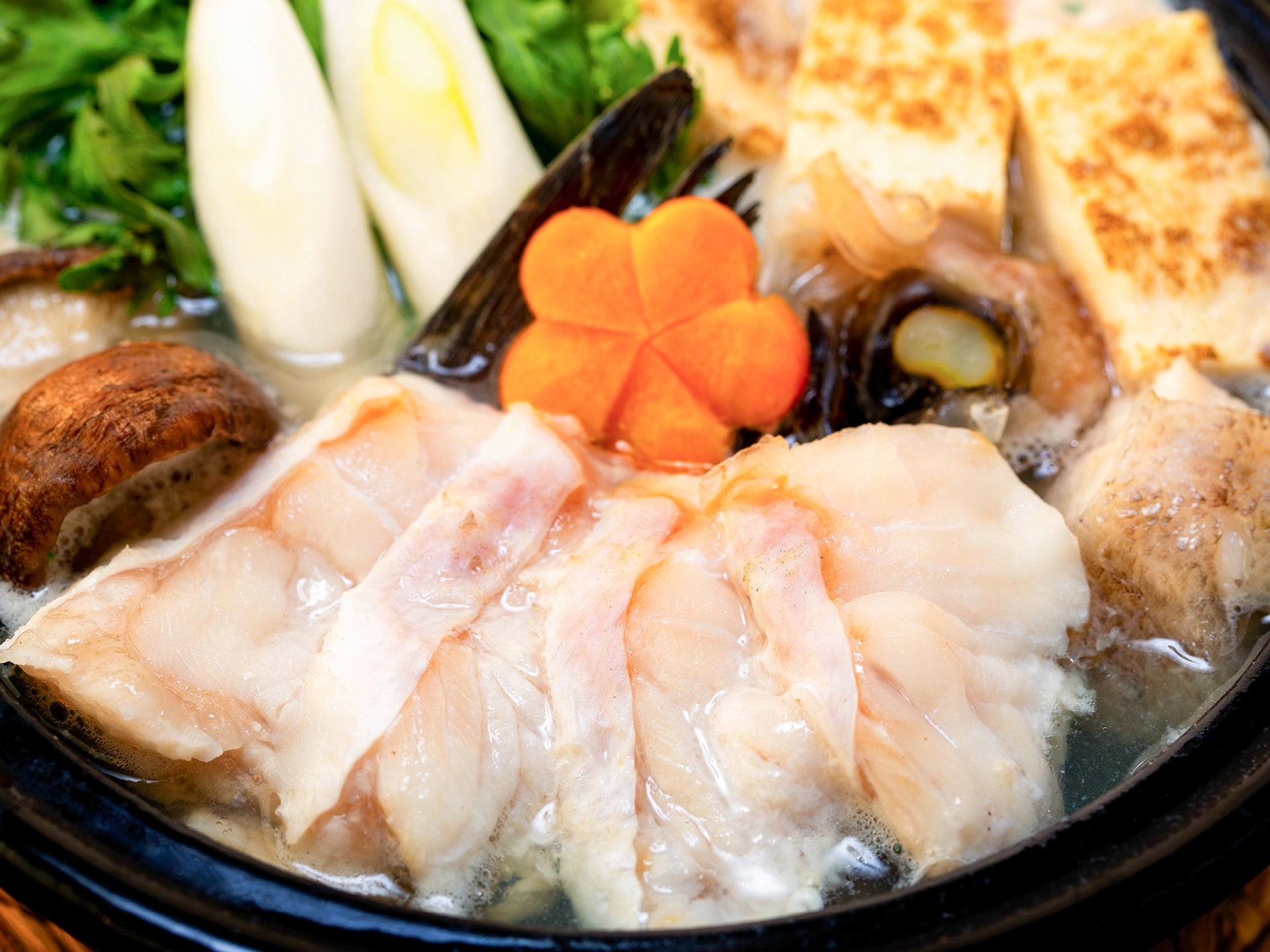 クエ鍋の調理写真。クエ、にんじん、ネギ、椎茸、豆腐などが写っている。